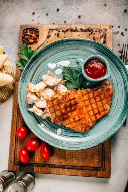 Patatesli ızgara biftek ve tabakta ketçap ve ahşap kesim tahtasında domatesler, yakın görüş. 