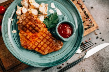 Patatesli ızgara biftek ve tabakta ketçap ve ahşap kesim tahtasında domatesler, yakın görüş. 