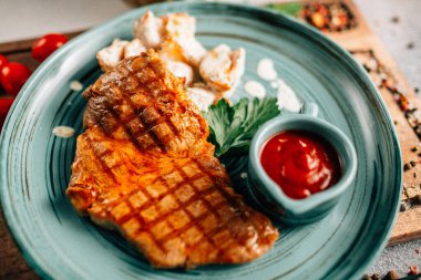 Patatesli ızgara biftek ve tabakta ketçap ve ahşap kesim tahtasında domatesler, yakın görüş. 