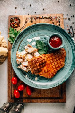 Patatesli ızgara biftek ve tabakta ketçap ve ahşap kesim tahtasında domatesler, yakın görüş. 
