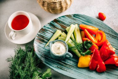 Taze kesilmiş sebze tabağı ve masada çay fincanı ile sos, yakın görüş. 