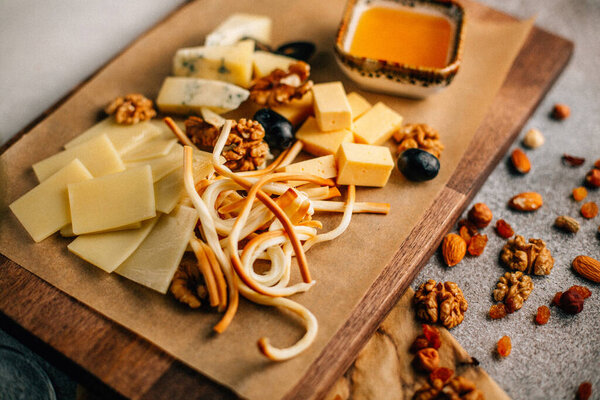 wooden board with cheese platter with grape and nuts with honey on table, close view 