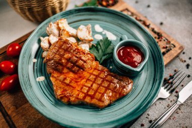 Patatesli ızgara biftek ve tabakta ketçap ahşap kesim tahtasında domatesler, yakın görüş. 