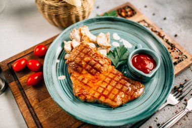 Patatesli ızgara biftek ve tabakta ketçap ahşap kesim tahtasında domatesler, yakın görüş. 