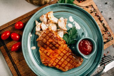 Patatesli ızgara biftek ve tabakta ketçap ahşap kesim tahtasında domatesler, yakın görüş. 