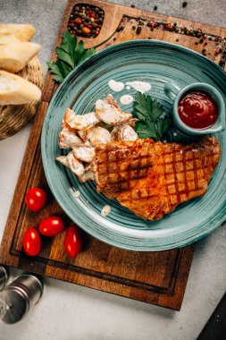 Patatesli ızgara biftek ve tabakta ketçap ahşap kesim tahtasında domatesler, yakın görüş. 