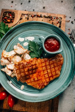 Patatesli ızgara biftek ve tabakta ketçap ahşap kesim tahtasında domatesler, yakın görüş. 