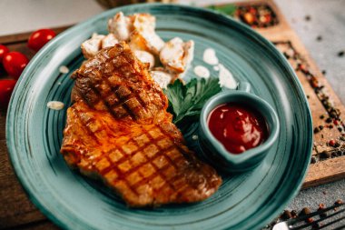 Patatesli ızgara biftek ve tabakta ketçap ahşap kesim tahtasında domatesler, yakın görüş. 