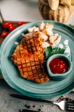 Patatesli ızgara biftek ve tabakta ketçap ahşap kesim tahtasında domatesler, yakın görüş. 