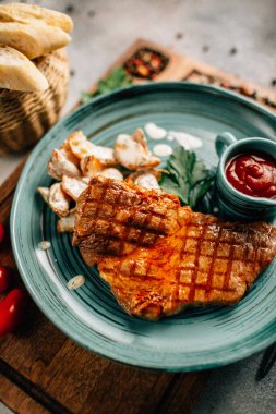 Patatesli ızgara biftek ve tabakta ketçap ahşap kesim tahtasında domatesler, yakın görüş. 