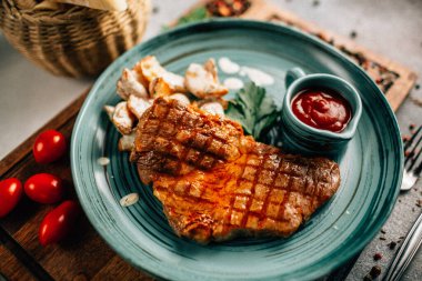 Patatesli ızgara biftek ve tabakta ketçap ahşap kesim tahtasında domatesler, yakın görüş. 