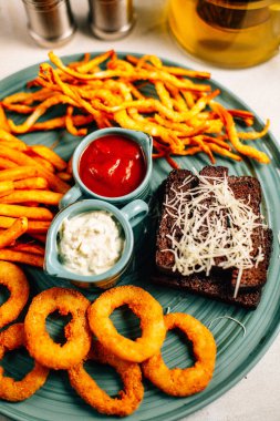 Kızarmış soğan halkalı bira tabağı ve kızarmış patates kızartması ile kalamar gevreği ve masada soslu kraker, yakın görüş.