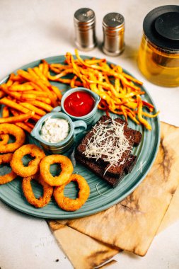 Kızarmış soğan halkalı bira tabağı ve kızarmış patates kızartması ile kalamar gevreği ve masada soslu kraker, yakın görüş.