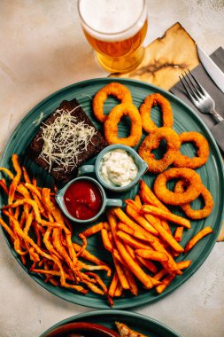 Kızarmış soğan halkalı bira tabağı ve kızarmış patates kızartması ile kalamar gevreği ve masada soslu kraker, yakın görüş.