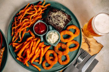 Kızarmış soğan halkalı bira tabağı ve kızarmış patates kızartması ile kalamar gevreği ve masada soslu kraker, yakın görüş.