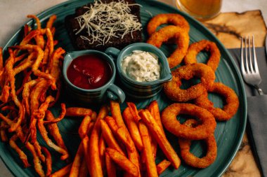 Kızarmış soğan halkalı bira tabağı ve kızarmış patates kızartması ile kalamar gevreği ve masada soslu kraker, yakın görüş.