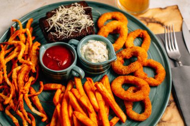 Kızarmış soğan halkalı bira tabağı ve kızarmış patates kızartması ile kalamar gevreği ve masada soslu kraker, yakın görüş.