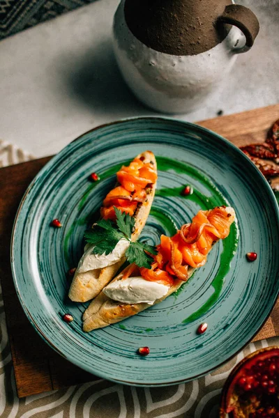 Mini bruschetta tabağı ve yumuşak mascarpone peynirli somon ve ahşap kesim tahtasının üzerinde nar tohumları. 