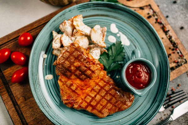 Patatesli ızgara biftek ve tabakta ketçap ahşap kesim tahtasında domatesler, yakın görüş. 