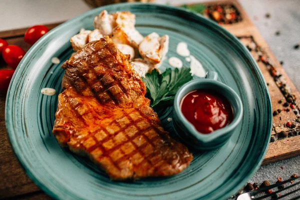 Patatesli ızgara biftek ve tabakta ketçap ahşap kesim tahtasında domatesler, yakın görüş. 