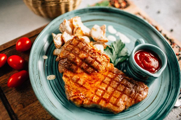 Patatesli ızgara biftek ve tabakta ketçap ahşap kesim tahtasında domatesler, yakın görüş. 