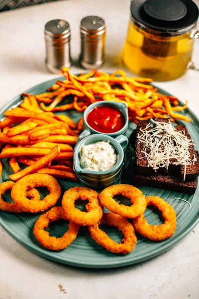 Kızarmış soğan halkalı bira tabağı ve kızarmış patates kızartması ile kalamar gevreği ve masada soslu kraker, yakın görüş.