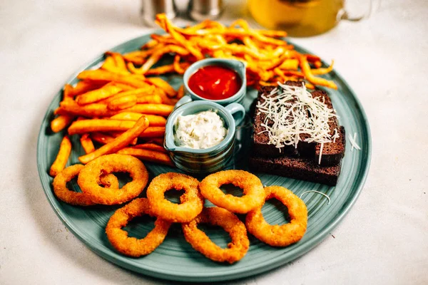 Kızarmış soğan halkalı bira tabağı ve kızarmış patates kızartması ile kalamar gevreği ve masada soslu kraker, yakın görüş.