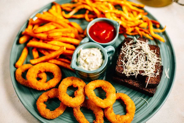 Kızarmış soğan halkalı bira tabağı ve kızarmış patates kızartması ile kalamar gevreği ve masada soslu kraker, yakın görüş.
