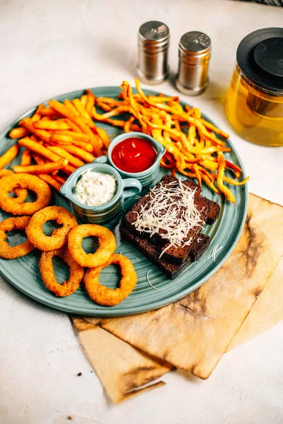 Kızarmış soğan halkalı bira tabağı ve kızarmış patates kızartması ile kalamar gevreği ve masada soslu kraker, yakın görüş.