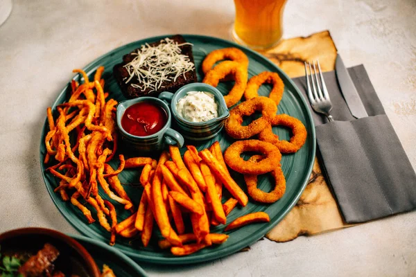 Kızarmış soğan halkalı bira tabağı ve kızarmış patates kızartması ile kalamar gevreği ve masada soslu kraker, yakın görüş.