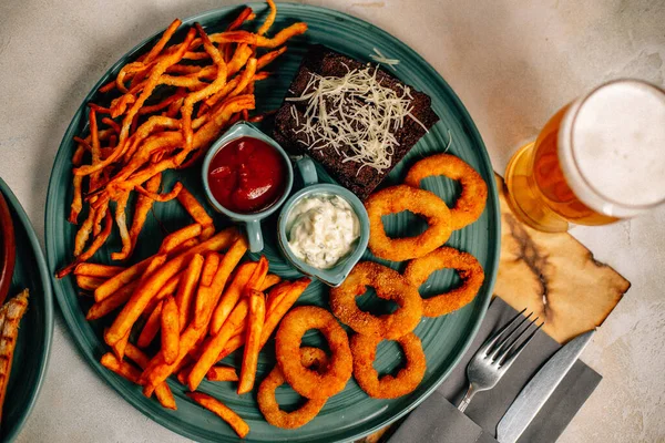 Kızarmış soğan halkalı bira tabağı ve kızarmış patates kızartması ile kalamar gevreği ve masada soslu kraker, yakın görüş.