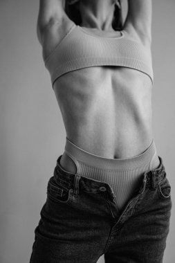 Spor iç çamaşırı giyen ve ışık stüdyosunda poz veren atletik vücutlu kadın modelin kırpılmış görüntüsü 