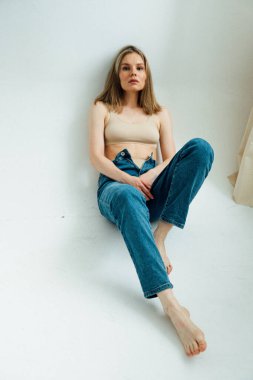 Spor iç çamaşırı ve kot pantolon giyen atletik vücutlu güzel bir kız ışık stüdyosunda poz veriyor. 