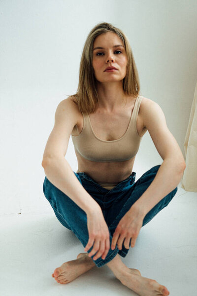 красивая девушка со спортивным телом в спортивном белье и джинсах позирует в легкой студии 