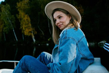 Güz ormanlarında gölde pedallı katamaran teknesinde oturan şık bir kot elbise giyen güzel bir kız.