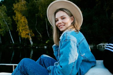 Güz ormanlarında gölde pedallı katamaran teknesinde oturan şık bir kot elbise giyen güzel bir kız.