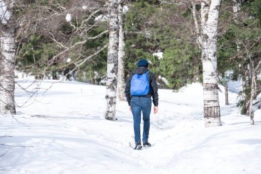 Genç bir adam ormanda güzel bir kış gününde patika boyunca yürür..