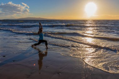 Gün batımında Maui sahilinde yoga yapan bir kadın.