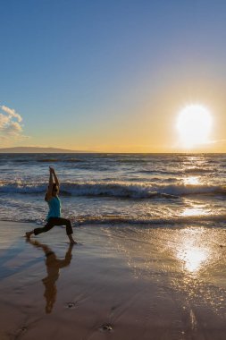 Gün batımında Maui sahilinde yoga yapan bir kadın.