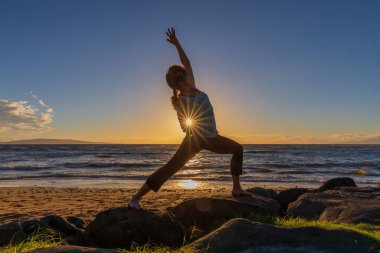 Gün batımında Maui sahilinde yoga yapan bir kadın.