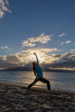 Gün batımında Maui sahilinde yoga yapan bir kadın.