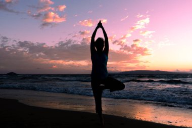 Maui sahilinde gün batımında yoga yapan bir kadın.