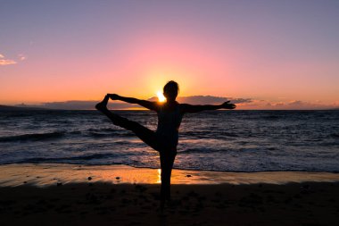 Maui sahilinde gün batımında yoga yapan bir kadın.