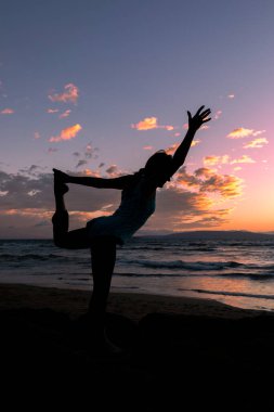 Maui sahilinde gün batımında yoga yapan bir kadın.