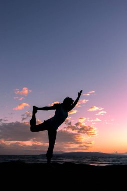 Maui sahilinde gün batımında yoga yapan bir kadın.