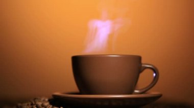 Sıcak bir içecek ve kahve taneleri, buhar, turuncu arka plan ile kahverengi Kupası.