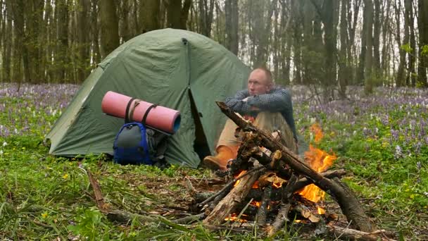 Mouvement lent à 100 FPS. Un adulte près d'un feu de camp et d'une tente pense à quelque chose . — Video