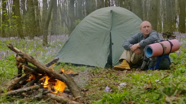 Повільний рух на 100 FPS. Дорослий сумний чоловік в лісі біля багаття і рюкзака . — стокове відео