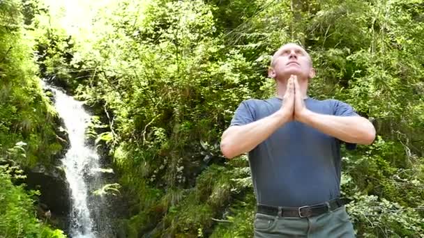 Al rallentatore. L'uomo fa meditazione vicino alla cascata. Cambiamento di obiettivo — Video Stock