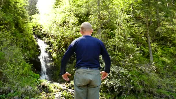 Медленное движение. Мужчина медитирует у водопада, руки вверх. Изменение фокуса — стоковое видео